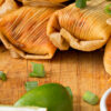 Avocado and hispanic foods next to a wooden platter filled with 7 of the best tamales online