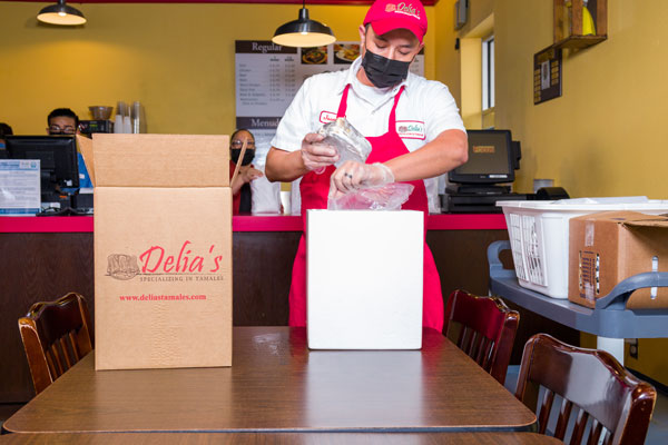 Worker with red apron preparing a box of tames for someone to order online.